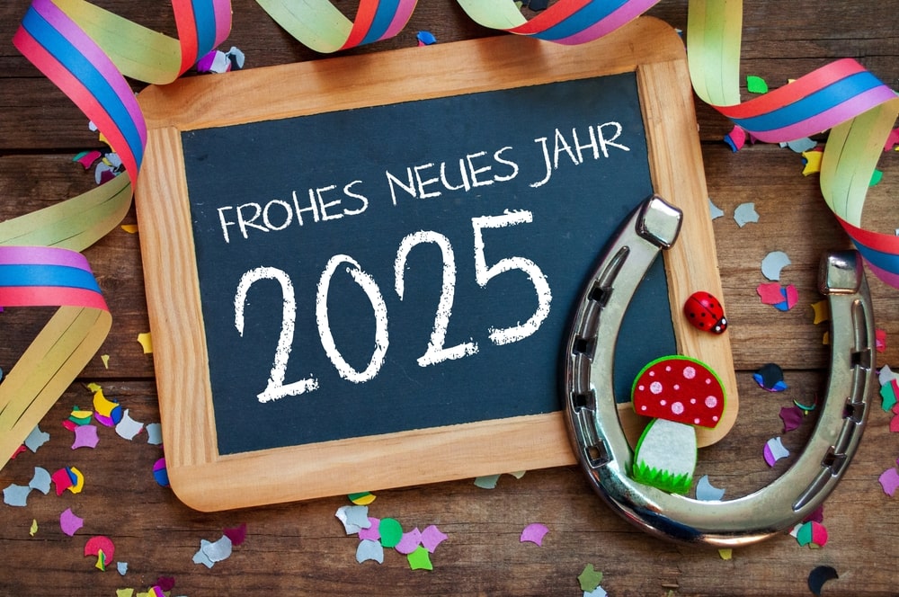 Eine kleine Tafel mit Holzrahmen liegt auf einem Holztisch. Auf der Tafel steht in weißer Schrift „Frohes neues Jahr 2025“.