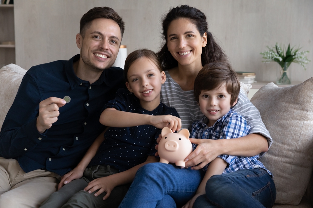 Familie sitzt auf Sofa und hält ein Sparschwein in der Hand.